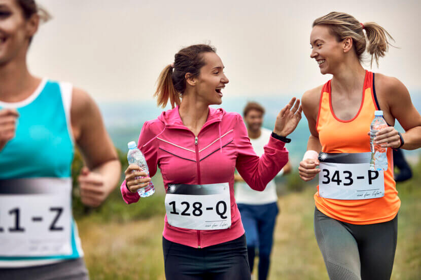Happy female runners communicating while participating in marathon in nature.