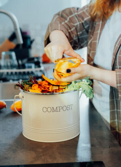 Compost the kitchen waste, recycling at home. Compost bin with vegetables cutted leftovers on the kitchen table with blurred woman cooking meal. Environmentally responsible, ecology. Selective focus