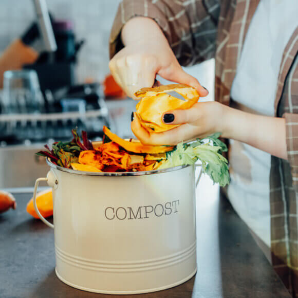 Composter les déchets de cuisine, trier à la maison. Bac à compost contenant des restes de légumes coupés sur la table de cuisine, avec une femme floue en train de préparer un repas. Respect de l'environnement, écologie. Plan d'ensemble
