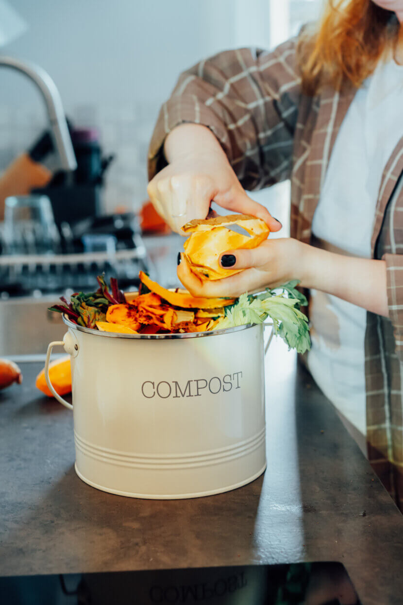 Composter les déchets de cuisine, trier à la maison. Bac à compost contenant des restes de légumes coupés sur la table de cuisine, avec une femme floue en train de préparer un repas. Respect de l'environnement, écologie. Plan d'ensemble