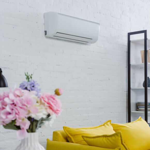 Interior of a modern living room with flowers in a vase, a yellow couch, and an air conditioner hanging on the wall