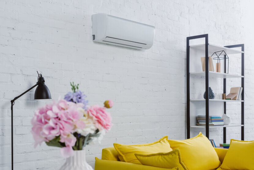Klimaanlage warten: Tipps für mehr Leistung und Effizienz interior of modern living room with flowers in vase, yellow couch and air conditioner hanging on