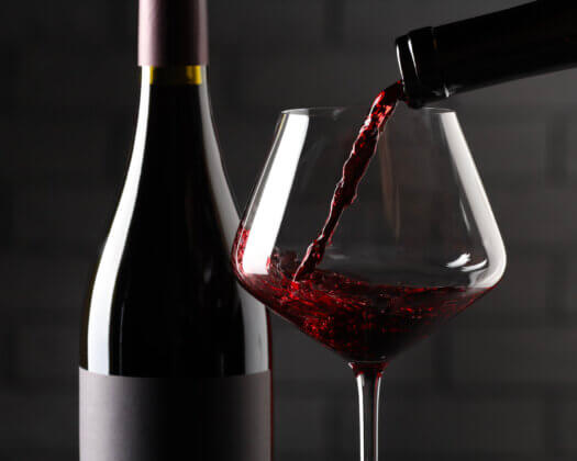 Pouring red wine into glass and bottles against brick wall background, closeup