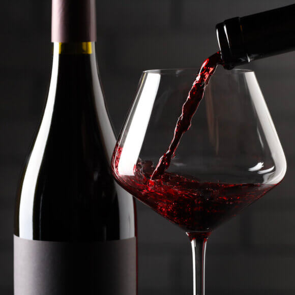 Gros plan sur du vin rouge versé dans des verres et des bouteilles, avec un mur de briques en arrière-plan