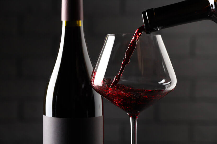 Wein richtig lagern: Die besten Plätze in der Wohnung Pouring red wine into glass and bottles against brick wall background, closeup