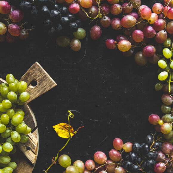 Assortment of fresh grape on cutting board. Grey wooden background.