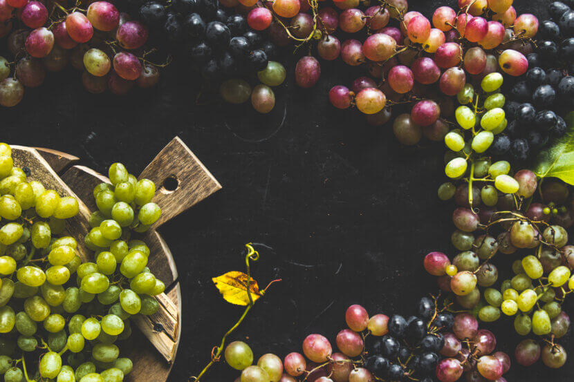 Assortment of fresh grape on cutting board. Grey wooden background.