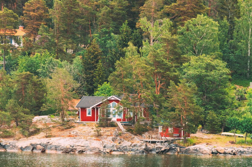 Climate change is reshaping the luxury real estate market: These regions are set to benefit Sweden. Beautiful red Swedish wooden log cabins on the rocky island coast in summer. Lake or river landscape