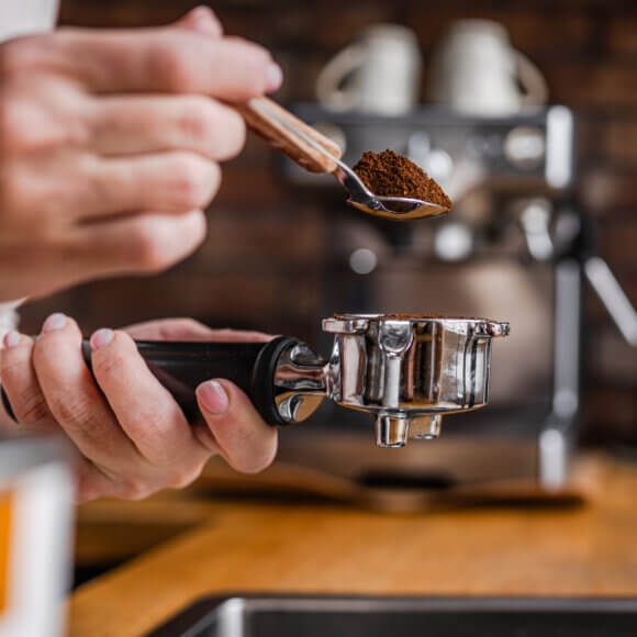 Une femme verse du café dans le porte-filtre d'une machine à expresso